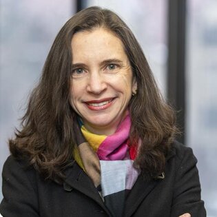 Smiling woman with long dark hair, dark coat and colorful scarf.